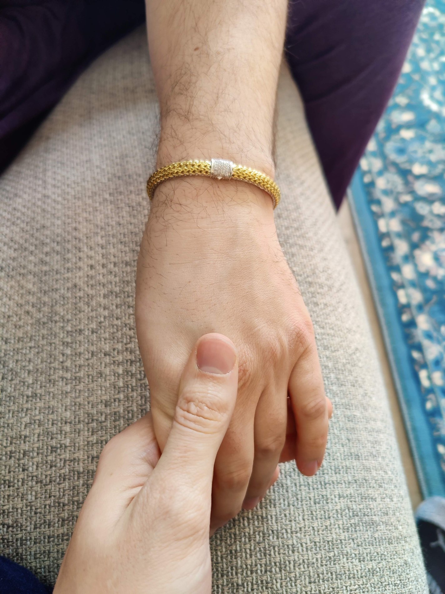 Two hands resting together, one wearing a gold bracelet