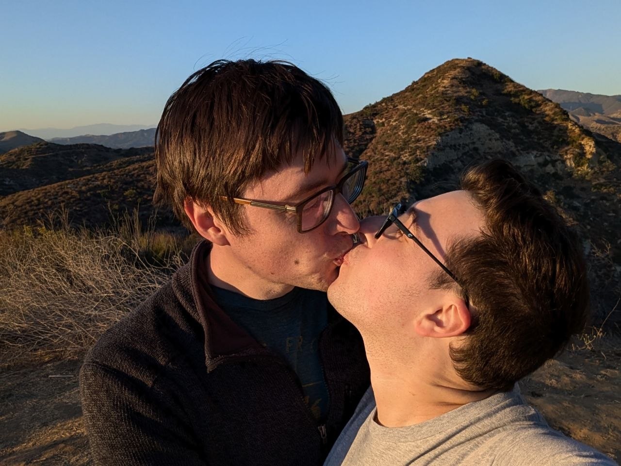Aaron and Peter kissing with sunlit hills behind them